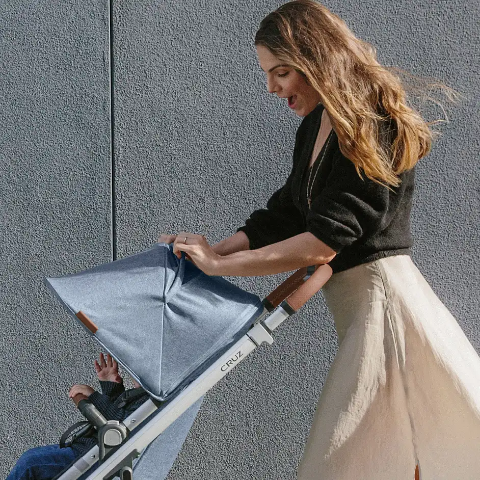 Mom strolling with child in Cruz V2, and flipping open peek a boo window for easy visibility to child