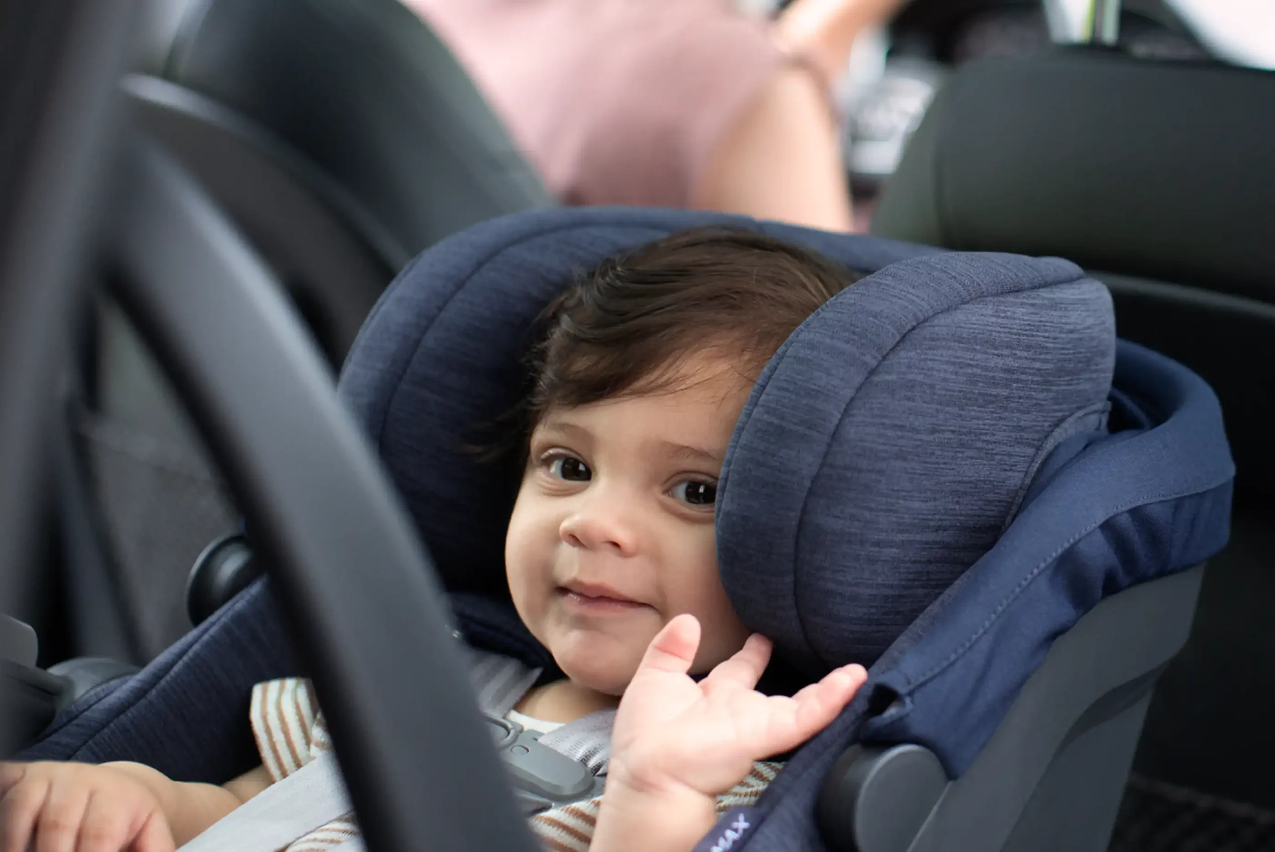 A child, safely secured in the Mesa Max infant car seat with its infinite adjustable headrest & Side Impact Protection, waves to their parent