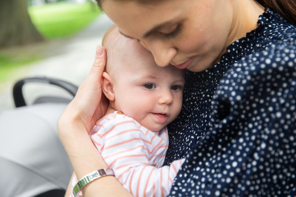 A mother holding her little one close, with an UPPAbaby Mesa V2 Infant car seat nearby.