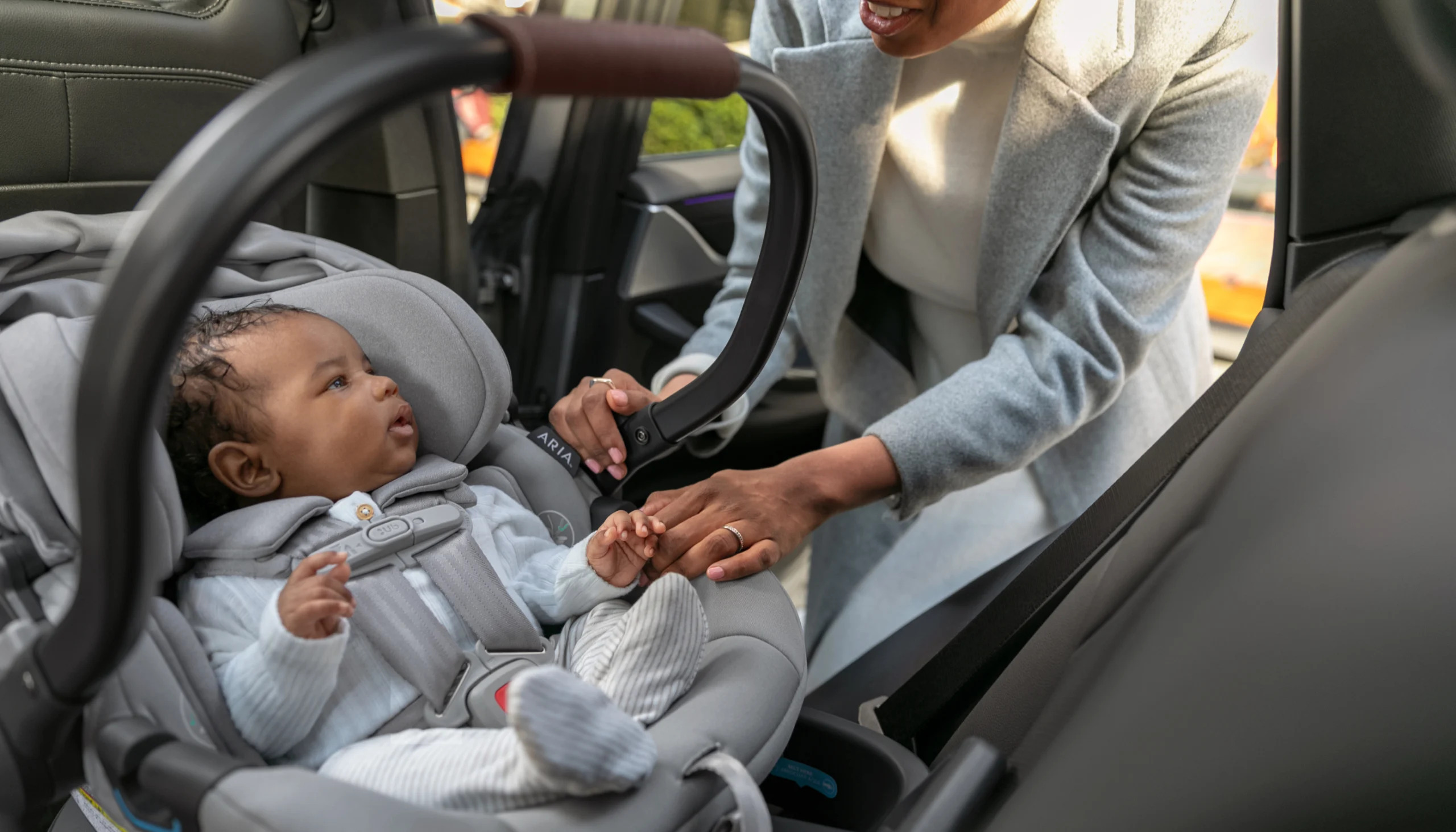 Baby in Aria infant car seat securely buckled into harness as mom looks in from car door