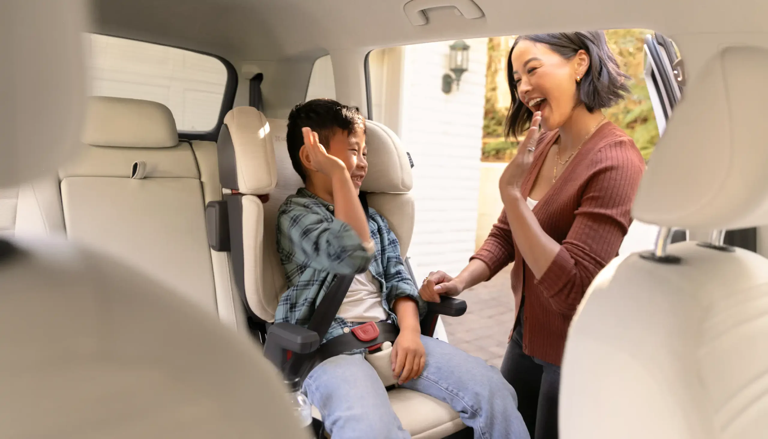 A smiling child high fives his mother in the slim Knox Convertible Car Seat, which is designed to maximize room within the vehicle and allow for more clearance for buckles imbedded into the seat cushion