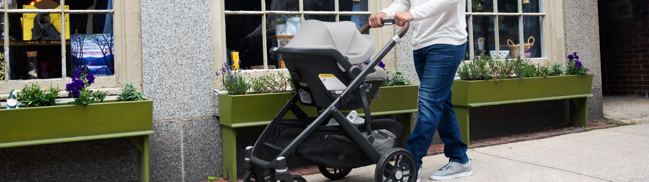 Man strolling his child in a Mesa car seat attached to a Vista V2 stroller past a storefront area.