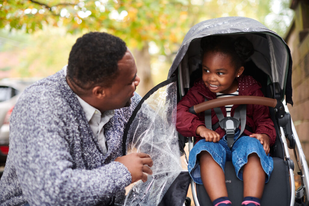 Smiling child in an UPPAbaby Vista V2 stroller under a clear rain shield, showcasing the brand's commitment to comfort and protection in all weather conditions