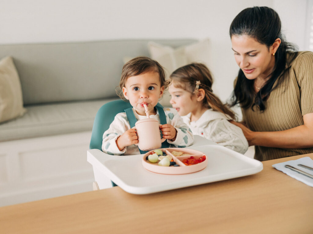 A child, secured in the comfortable Ciro high chair, participates in mealtime with their family, eating and giggling with everyone else