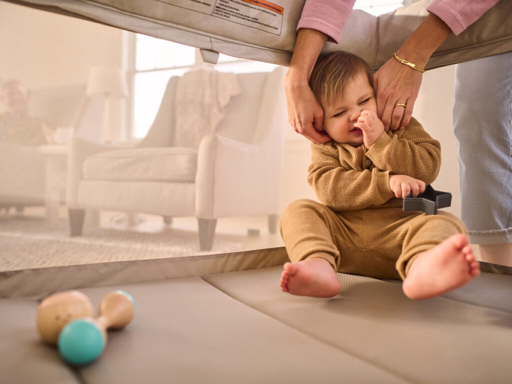 A baby giggles as their caretaker tends to baby within the Remi playard