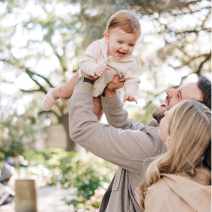 Child laughs as parents playfully raise him into the air