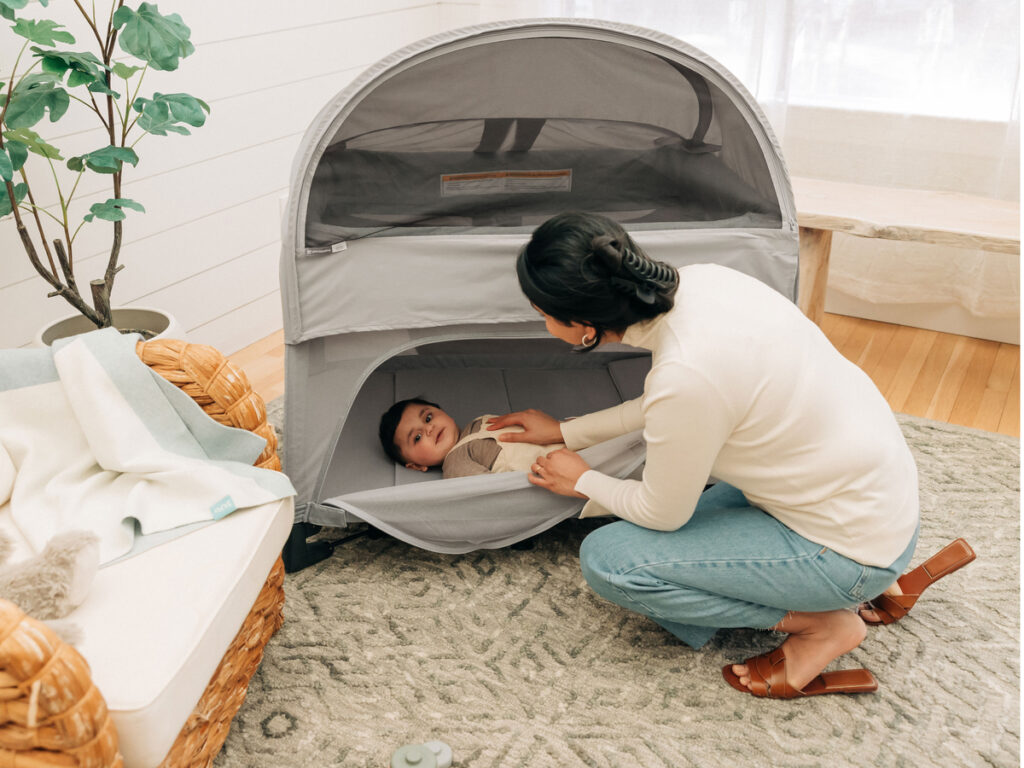 Mother reaches for baby laying in Remi with Canopy accessory