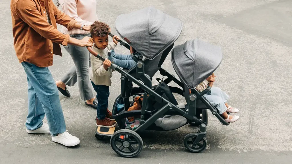 Parents push children in a Vista V3 with a child in the Toddler Seat, RumbleSeat, and standing on the PiggyBack